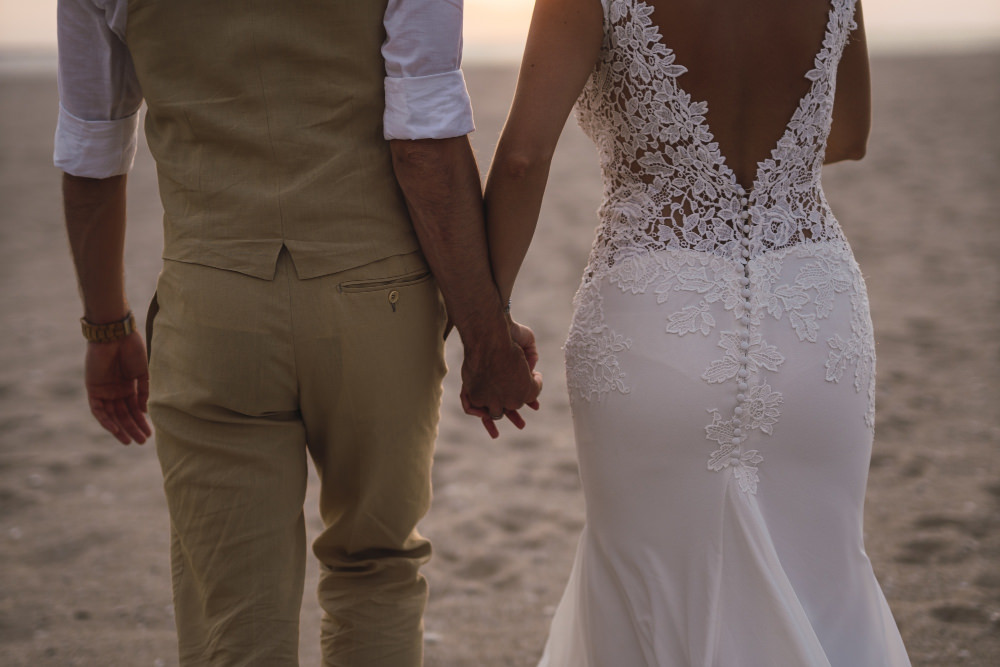 Novios con ropa de boda paseando por la arena de la playa